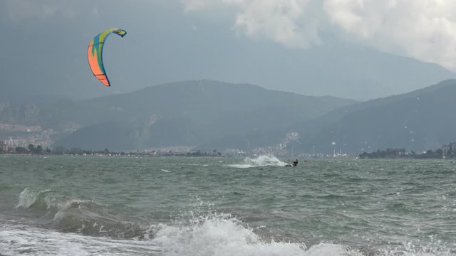 Fethiye, Turkey - 27th of Martch 2020: 4K In stormy weather a Kitesurfer approaches riding along the beach, zoom out
