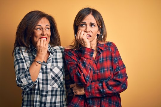Middle age beautiful couple of sisters wearing casual shirt over isolated yellow background looking stressed and nervous with hands on mouth biting nails. Anxiety problem.
