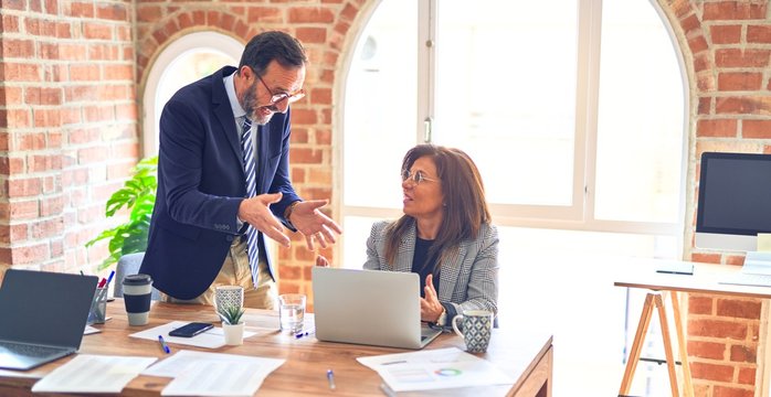 Two middle age business workers working together. Man bullying woman at the office