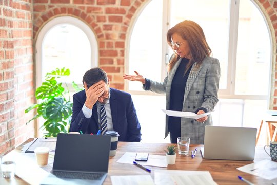 Two middle age business workers working together. Woman bullying man at the office