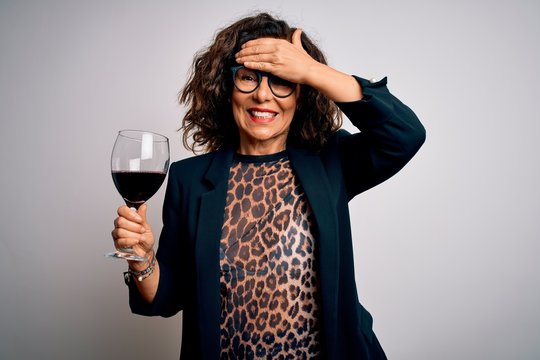 Middle age brunette woman drinking glass of red wine over isolated white background stressed with hand on head, shocked with shame and surprise face, angry and frustrated. Fear and upset for mistake.