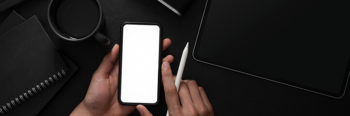 Overhead shot of a man holding blank screen smartphone in dark modern concept workspace