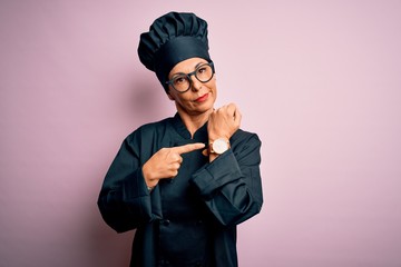 Middle age brunette chef woman wearing cooker uniform and hat over isolated pink background In...
