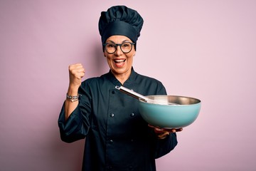 Middle age brunette chef woman wearing cooker uniform and hat using whisk and bowl screaming proud...