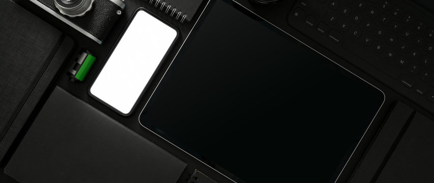 Top view of dark workspace with mock-up smartphone, tablet and photographer supplies
