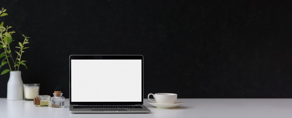 Cropped shot of dark modern concept workspace with copy space, mock-up laptop, coffee cup and decorations