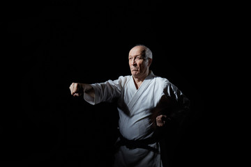 The old athlete trains a punch on a black background