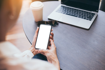 Mockup image blank white screen cell phone.woman hand holding texting using mobile on desk at coffee shop.background empty space for advertise text.people contact marketing business,technology