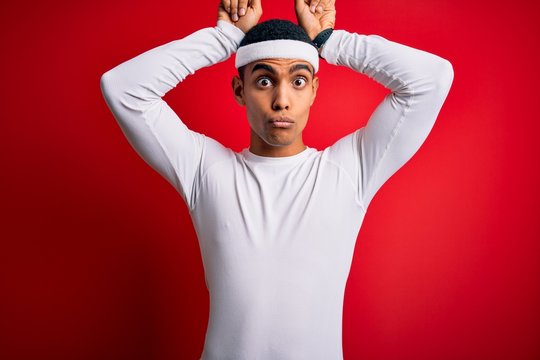 Young handsome african american sportsman wearing sportswear over red background doing funny gesture with finger over head as bull horns