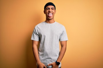 Handsome african american sportsman doing sport wearing sportswear over yellow background sticking tongue out happy with funny expression. Emotion concept.