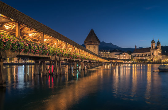 Night time shot of the iconic medieval Lucerne Chapel footbridge running along the River Reuss with the water tower and city lights with town buildings in the background. This wooden bridge is the wor