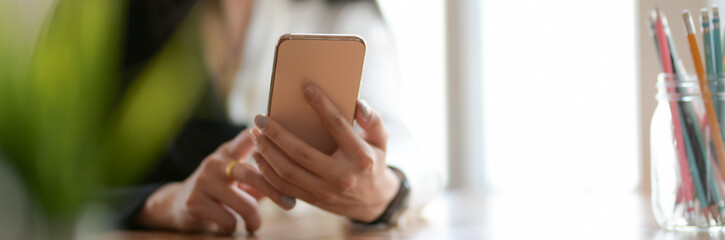 Cropped shot of female freelancer using smartphone to relax form her work