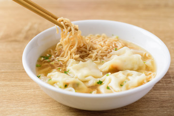 Instant noodles soup and wonton dumpling stuffed with minced pork in a bowl eating by chopsticks,...