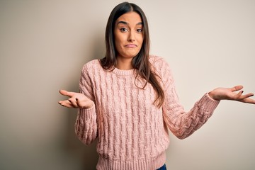Young beautiful brunette woman wearing casual sweater over isolated white background clueless and...
