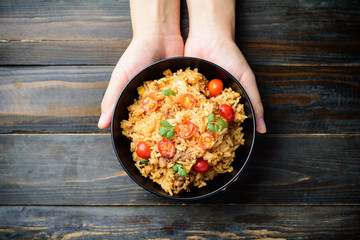 Fried rice with minced pork and tomato in a bowl holding by hand on wooden background, Asian food