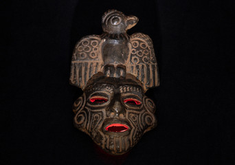 An ancient ceramic pre columbus mask based in American indigenous tribes art iluminated by red light inside and white light over black background 