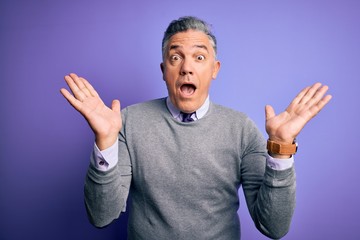 Fototapeta premium Middle age handsome grey-haired man wearing elegant sweater over purple background celebrating crazy and amazed for success with arms raised and open eyes screaming excited. Winner concept