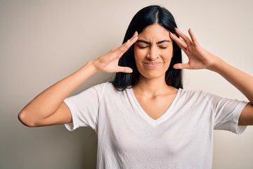Young beautiful hispanic woman wearing casual white t-shirt over isolated background suffering from headache desperate and stressed because pain and migraine. Hands on head.