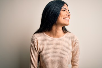 Young beautiful hispanic woman wearing elegant pink sweater over isolated background looking away to side with smile on face, natural expression. Laughing confident.