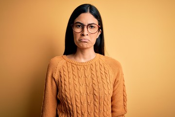 Young beautiful hispanic woman wearing glasses over yellow isolated background depressed and worry for distress, crying angry and afraid. Sad expression.