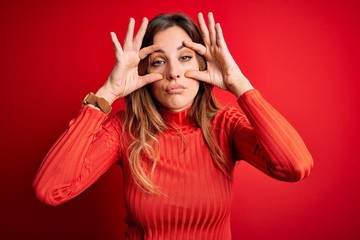 Young beautiful brunette woman wearing casual turtleneck sweater over red background Trying to open eyes with fingers, sleepy and tired for morning fatigue