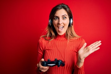 Young beautiful brunette gamer woman playing video game using joystic and headphones very happy and excited, winner expression celebrating victory screaming with big smile and raised hands