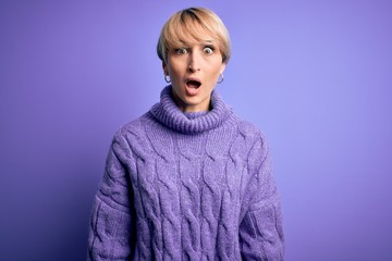 Young blonde woman with short hair wearing winter turtleneck sweater over purple background afraid and shocked with surprise and amazed expression, fear and excited face.