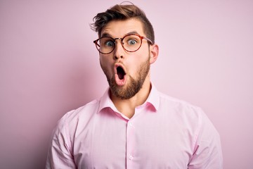 Obraz premium Young handsome blond man with beard and blue eyes wearing pink shirt and glasses afraid and shocked with surprise expression, fear and excited face.