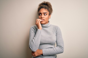 Beautiful african american girl wearing turtleneck sweater standing over white background looking stressed and nervous with hands on mouth biting nails. Anxiety problem.