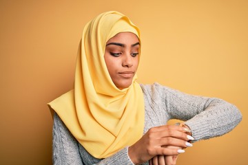 Young beautiful african american girl wearing muslim hijab over isolated yellow background Checking the time on wrist watch, relaxed and confident