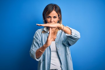 Middle age beautiful woman wearing casual shirt standing over isolated blue background Doing time out gesture with hands, frustrated and serious face