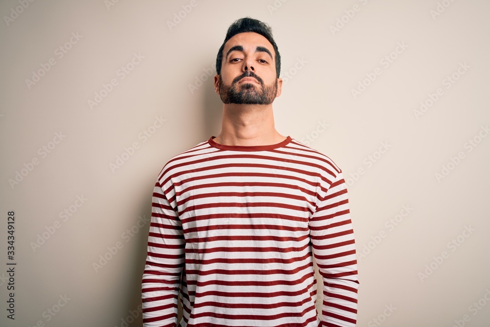 Poster Young handsome man with beard wearing casual striped t-shirt standing over white background Relaxed with serious expression on face. Simple and natural looking at the camera.