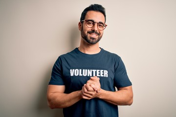 Handsome man with beard wearing t-shirt with volunteer message over white background with hands together and crossed fingers smiling relaxed and cheerful. Success and optimistic