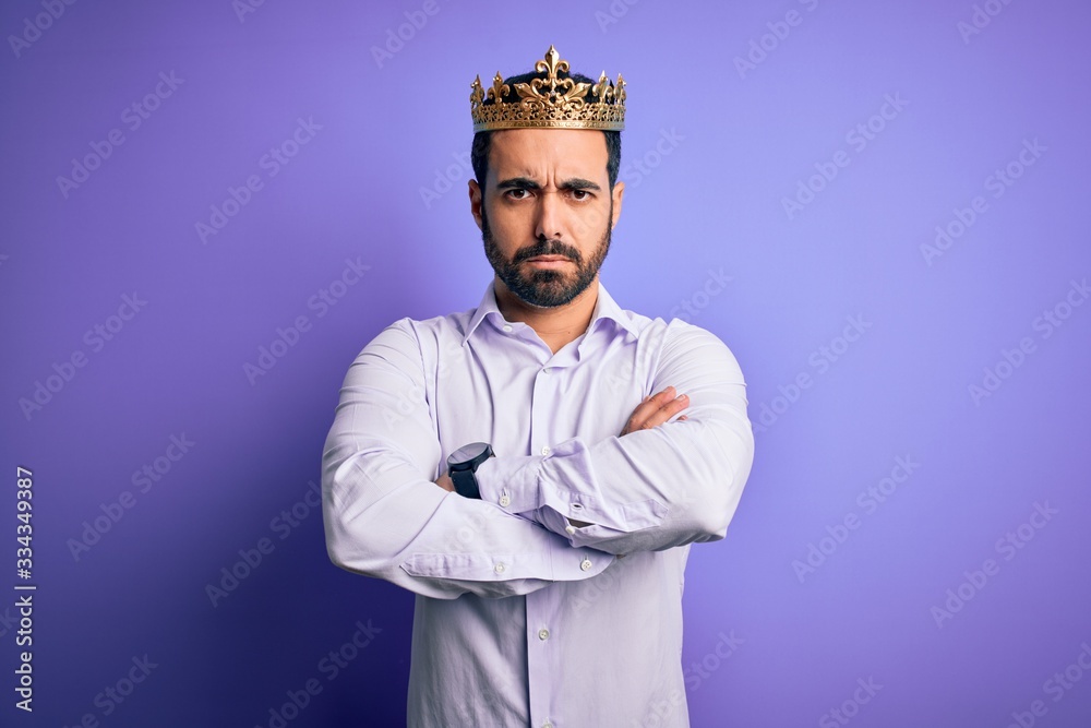 Poster Young handsome man with beard wearing golden crown of king over purple background skeptic and nervous, disapproving expression on face with crossed arms. Negative person.