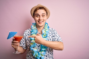 Young redhead tourist man on vacation wearing hat and hawaiian lei drinking cocktail Smiling happy pointing with hand and finger