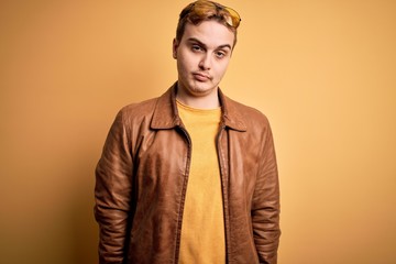 Young handsome redhead man wearing casual leather jacket over isolated yellow background looking sleepy and tired, exhausted for fatigue and hangover, lazy eyes in the morning.