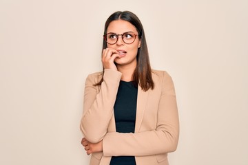 Young beautiful brunette businesswoman wearing jacket and glasses over white background looking stressed and nervous with hands on mouth biting nails. Anxiety problem.