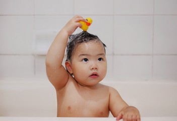 A cute Asian girl playing a yellow rubber ducky in a bathtub, happy, laughing and smiling.