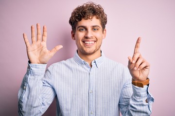 Young blond handsome man with curly hair wearing striped shirt over white background showing and pointing up with fingers number six while smiling confident and happy.