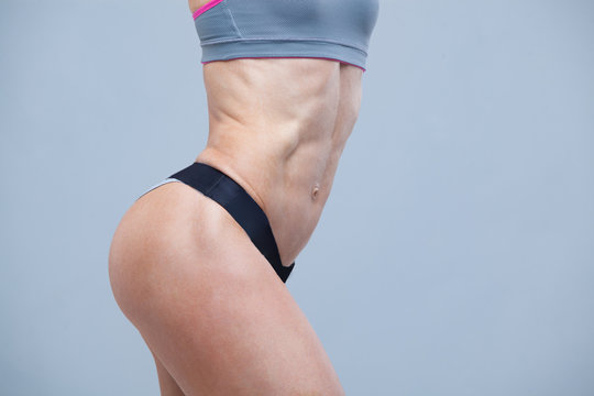 Close-up of the abdominal muscles of young girl athlete on grey background
