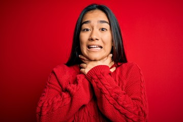 Young beautiful asian woman wearing casual sweater standing over isolated red background shouting and suffocate because painful strangle. Health problem. Asphyxiate and suicide concept.