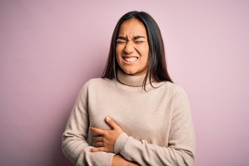 Young beautiful asian woman wearing casual turtleneck sweater over pink background with hand on stomach because nausea, painful disease feeling unwell. Ache concept.