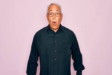 Middle age senior grey-haired handsome man wearing glasses and elegant shirt afraid and shocked with surprise expression, fear and excited face.