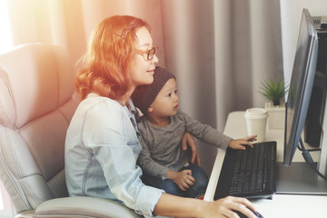 Young mother in home office with computer and her son