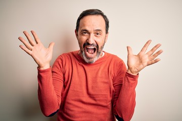 Middle age hoary man wearing casual orange sweater standing over isolated white background celebrating crazy and amazed for success with arms raised and open eyes screaming excited. Winner concept