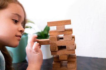 Cute girl is building a tower out of wooden blocks. Development fine motor skills in children. Child knows how to think and reason logically. Closeup of player kid