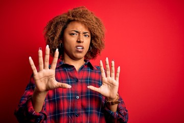 Young beautiful African American afro woman with curly hair wearing casual shirt afraid and terrified with fear expression stop gesture with hands, shouting in shock. Panic concept.