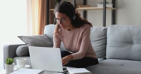 Millennial woman wearing headset making video chat working from home using laptop. Young female online teacher conferencing on business call communicating by webcam on computer. Distance telework. - Powered by Adobe