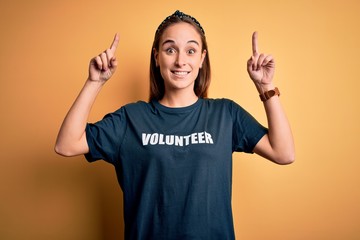 Young beautiful woman wearing volunteer t-shirt doing volunteering over yellow background smiling...