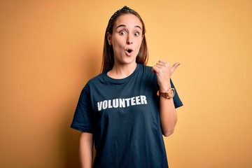 Young beautiful woman wearing volunteer t-shirt doing volunteering over yellow background Surprised...
